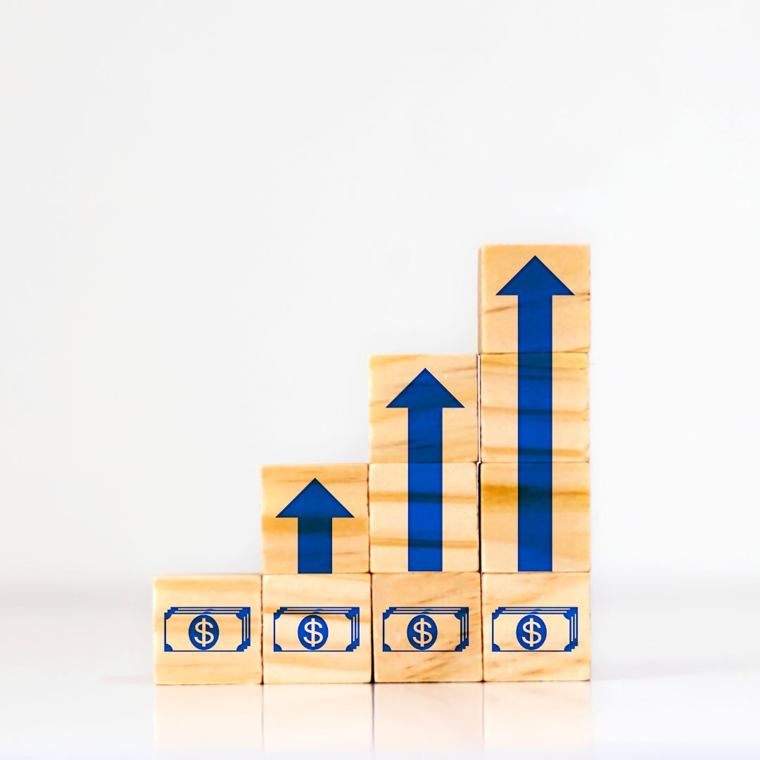 Wooden blocks arranged in ascending order with blue upward arrows and dollar symbols, symbolizing business growth and financial success.