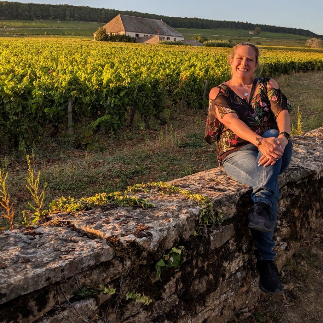 Kristen David, CEO of Upleveling Your Business, sitting on a stone wall in France