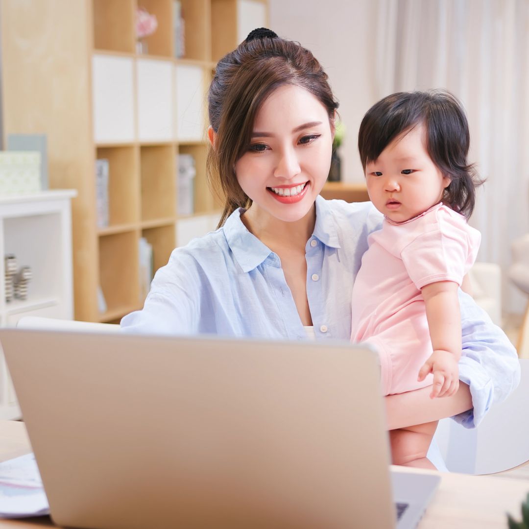 A mother holding her baby and working on a laptop