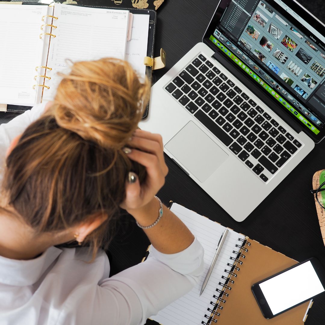 A stressed woman with papers and a laptop on her desk