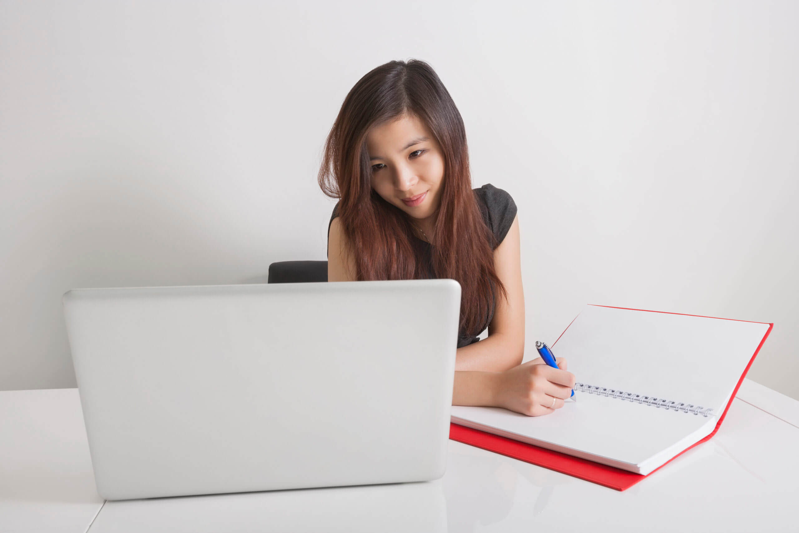 Young woman studying and taking notes while using a laptop, illustrating the process of learning and implementing business systems.