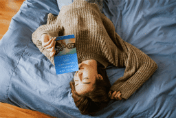 Woman relaxing on a bed while reading "Uplevel Your Business, Uplevel Your Life," a book by Kristen David, promoting effective business management and team building.
