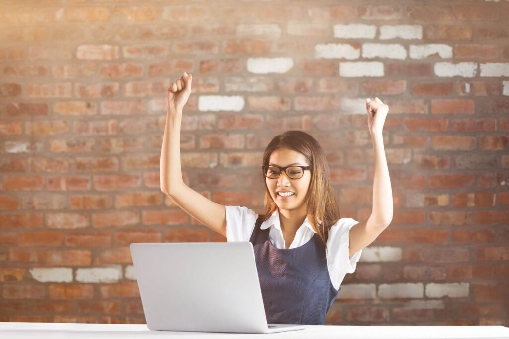 Woman celebrating success while working on a laptop, symbolizing business growth and strategy development for Upleveling Your Business coaching services.