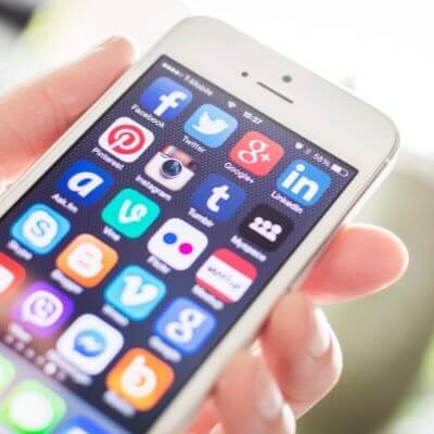 Hand holding smartphone displaying various social media app icons, relevant to marketing and content creation strategies.