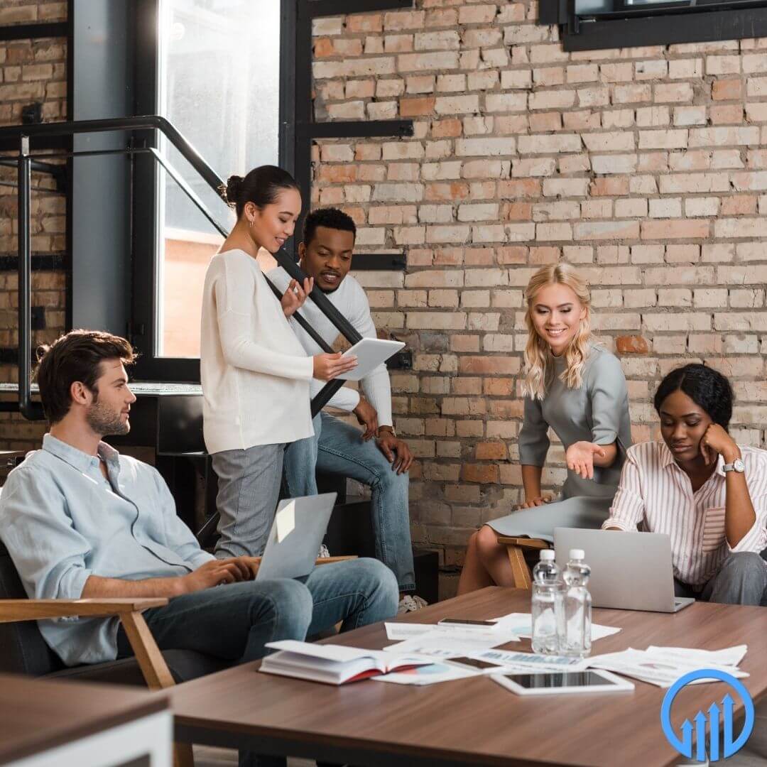 Group of diverse professionals collaborating in a modern office setting, discussing business strategies with laptops and documents on a table.