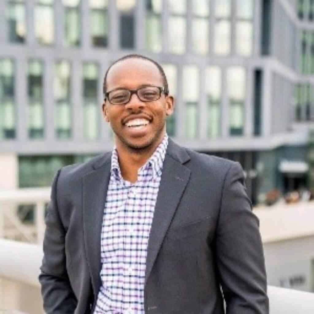 Coach Terrell Turner smiling in a professional setting, wearing a blazer and a checkered shirt, representing financial coaching and business growth.