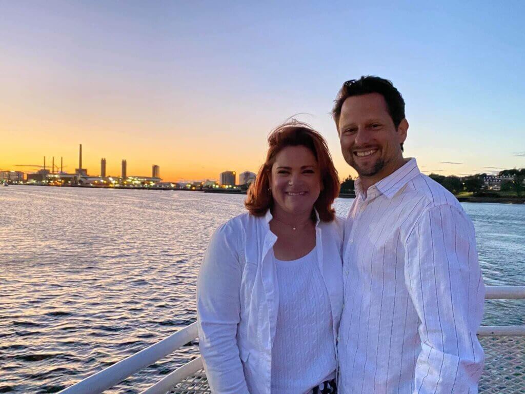 Jaclyn DuBois-Zolnik and her husband smiling together at sunset by the water, embodying a personal connection and balance in life outside her coaching profession.