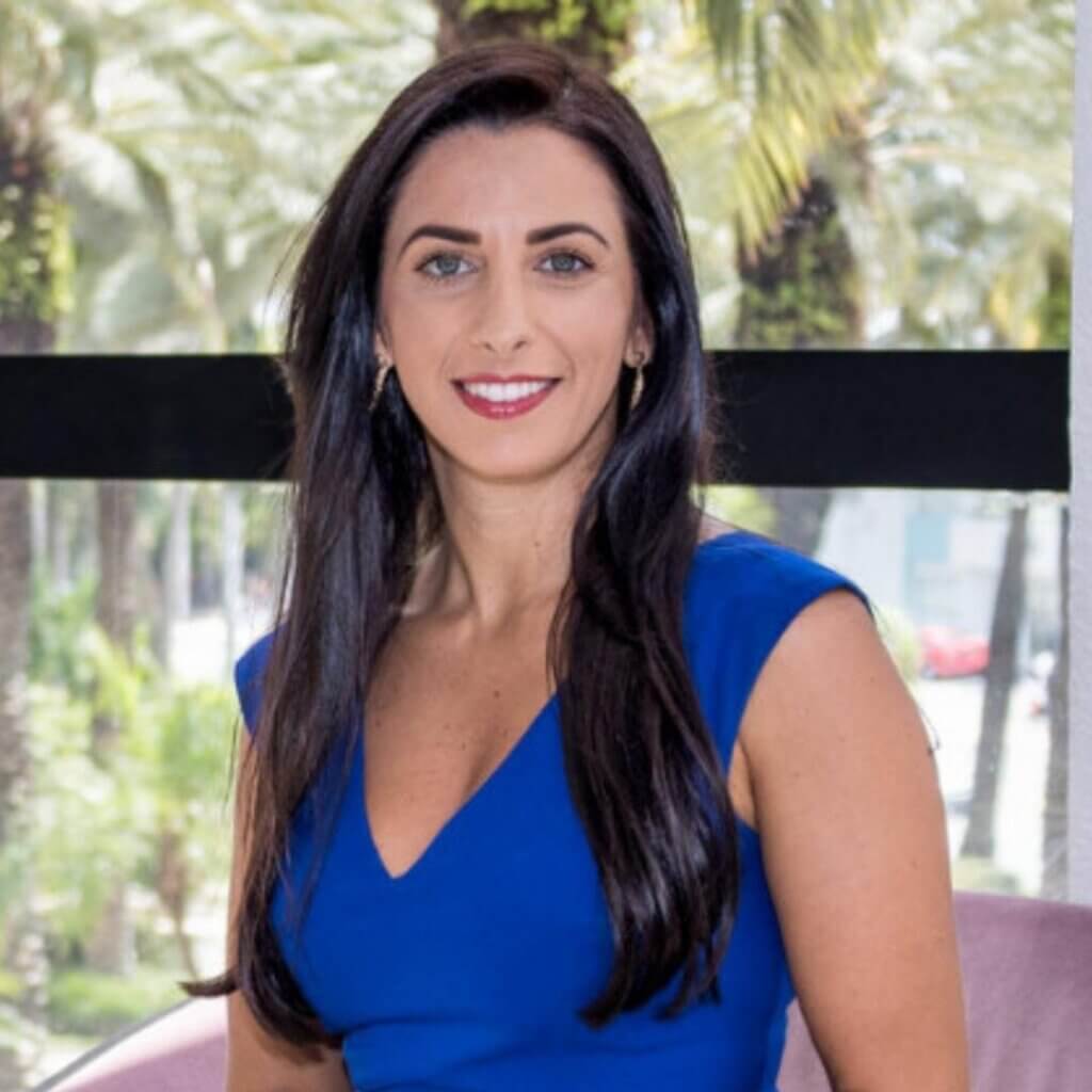 Caline Assilian, Culture and Management Coach, smiling in a blue dress, with a background of palm trees and urban scenery, representing her expertise in business development and coaching.