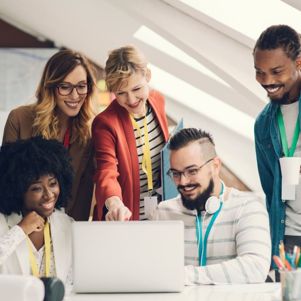 Group of diverse professionals collaborating around a laptop, engaged in training and teamwork for business growth during Upleveling Your Business Implementation Boot Camps.