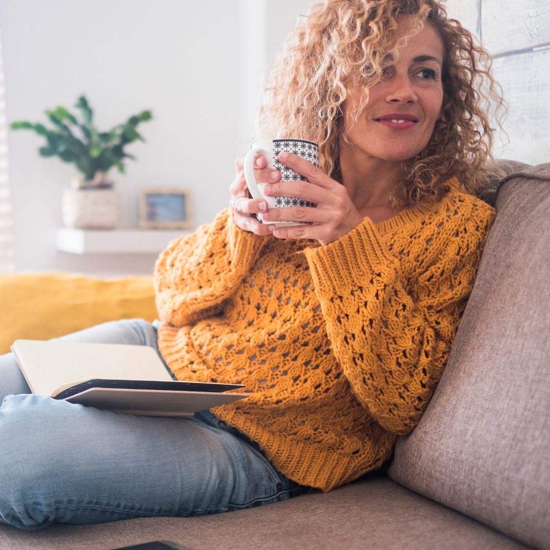 smiling woman in a yellow sweater holding a cup of coffee and reading a book