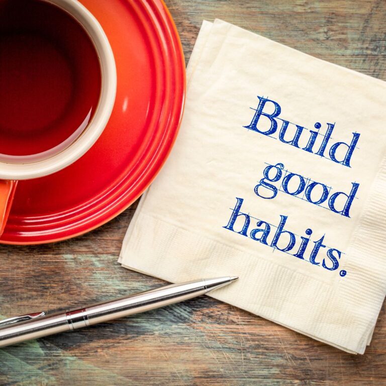 red mug and saucer with a napkin and the message "build good habits."