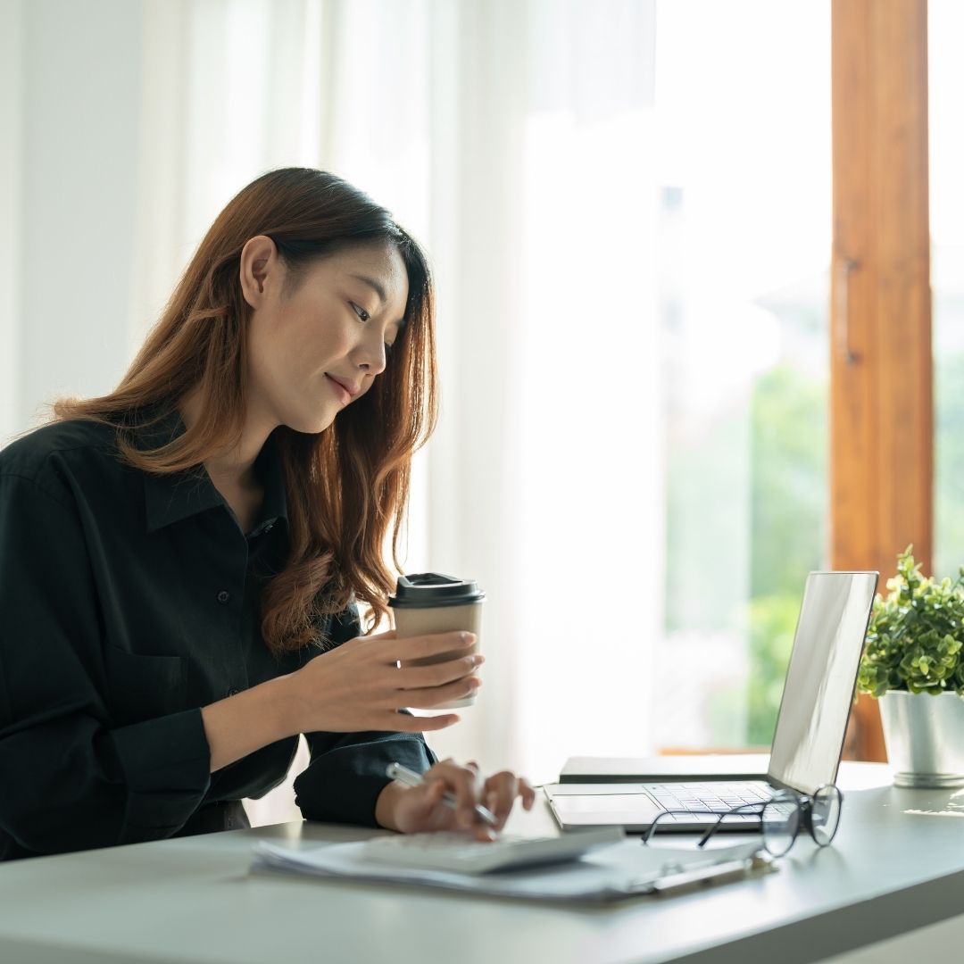 business woman holding a cup of coffee and working at a laptop