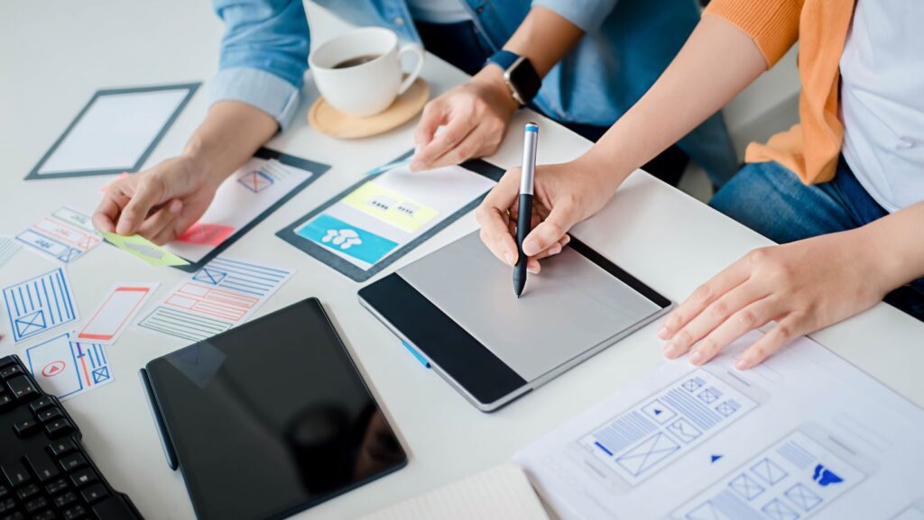 Team collaborating on marketing strategy, using tablet and sketches, with coffee cup in background, illustrating hands-on approach to training and resources in Marketing Boot Camp.
