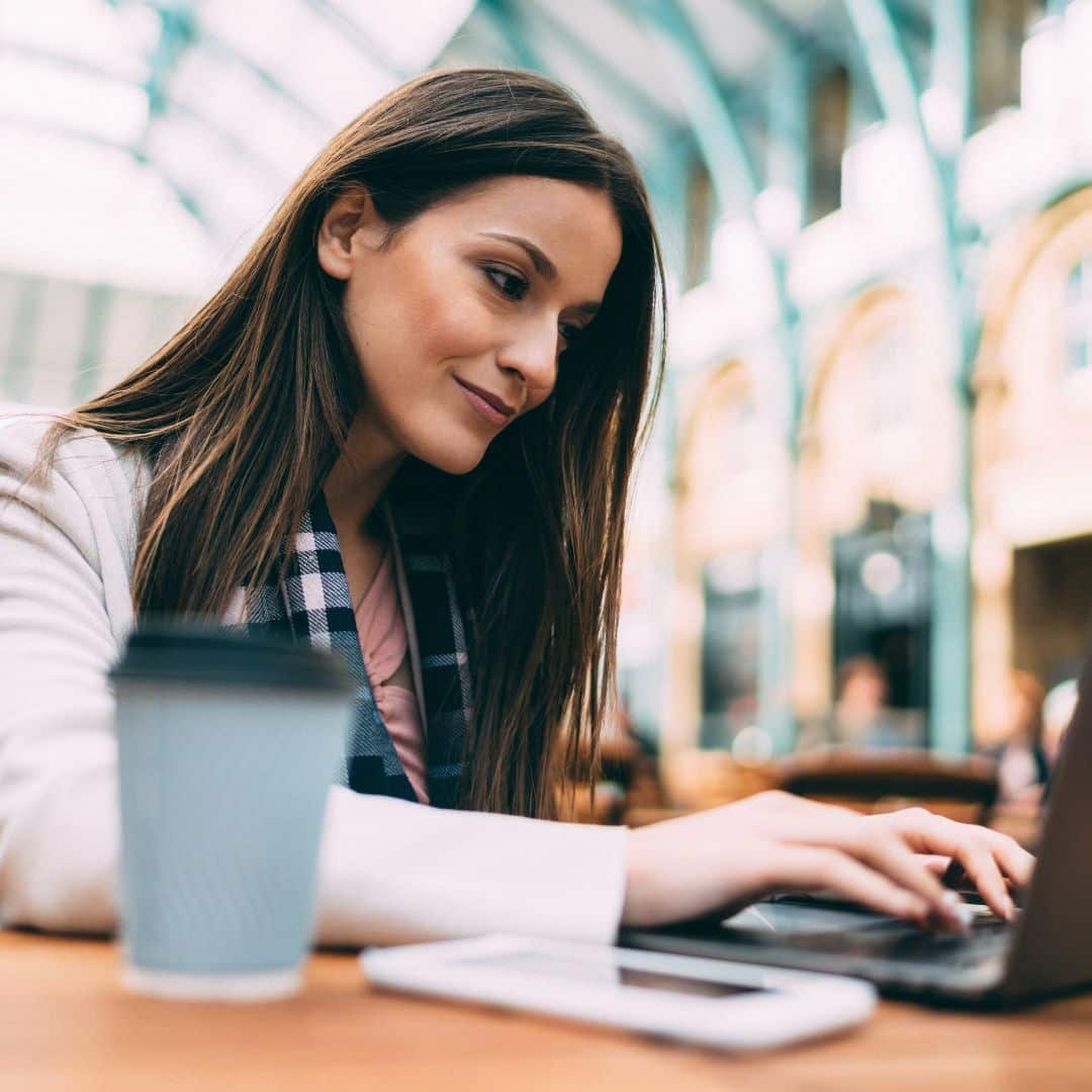 Woman typing on laptop in a café, with a coffee cup and smartphone nearby, symbolizing focused planning and productivity for entrepreneurs at year-end.