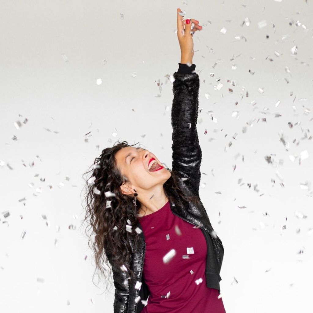Woman celebrating with raised arm in confetti, embodying confidence and success, reflecting themes of leadership and data-driven decision-making from the Upleveling Your Business workshop.