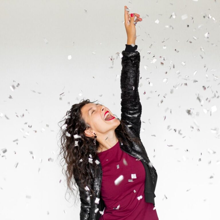 A joyful woman in a purple top and black jacket celebrating with confetti