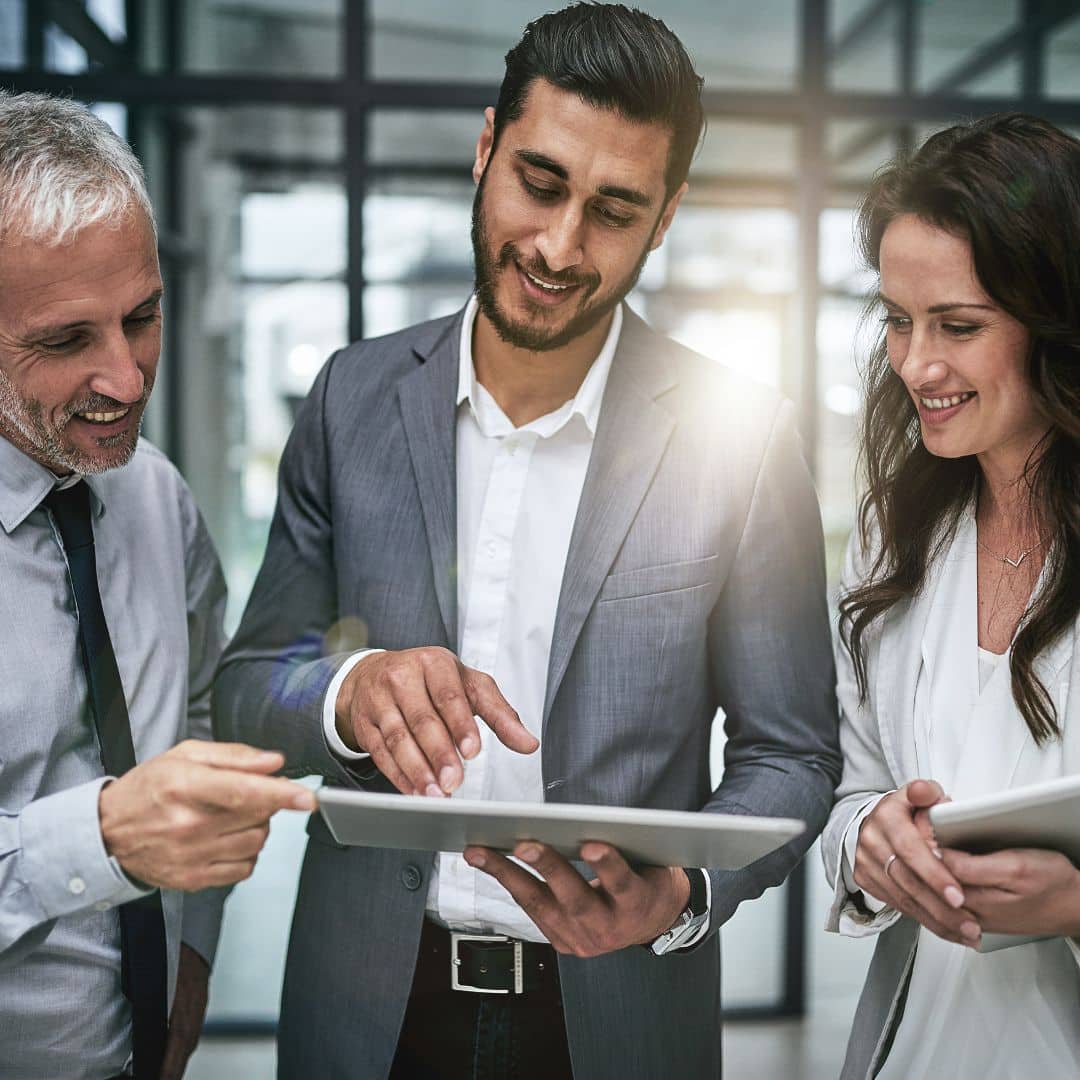 Three business professionals collaborating, discussing a digital tablet, in a modern office setting, reflecting teamwork and planning for year-end evaluations and future goals.