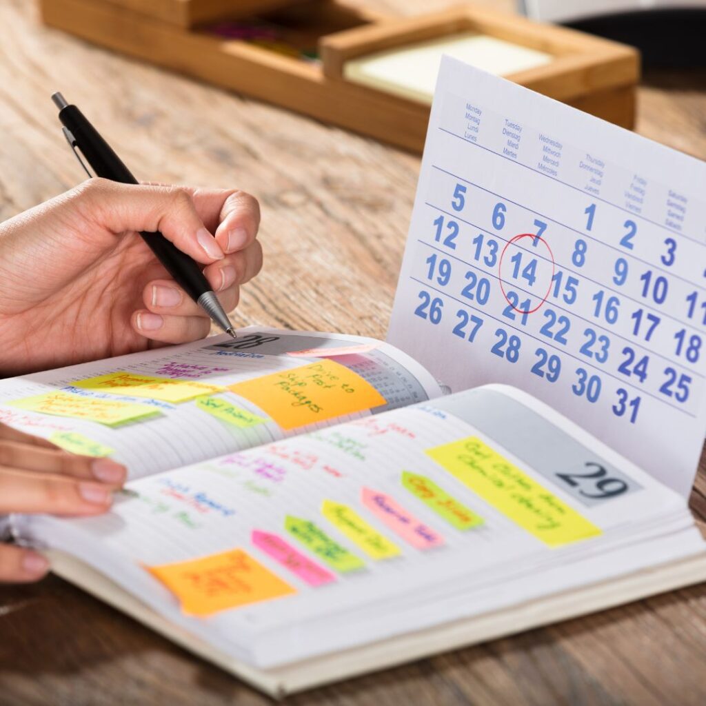 Person writing in a planner with colorful sticky notes and a calendar, representing marketing planning and organization for effective team strategies.