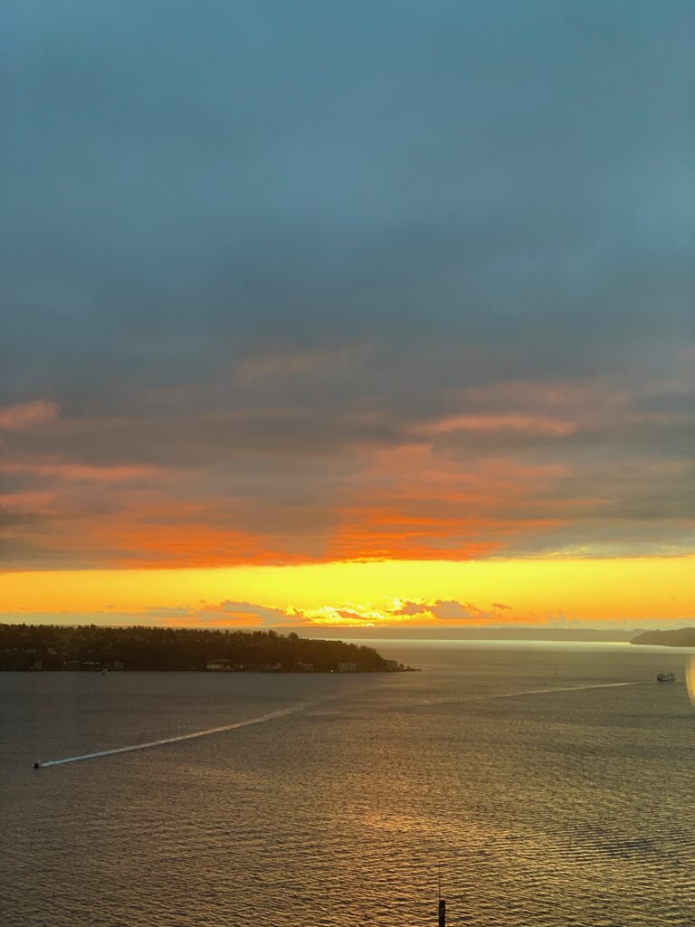 Sunset over calm water with orange and yellow hues, reflecting on the surface, and a distant shoreline visible, symbolizing new beginnings and transitions in a professional context.