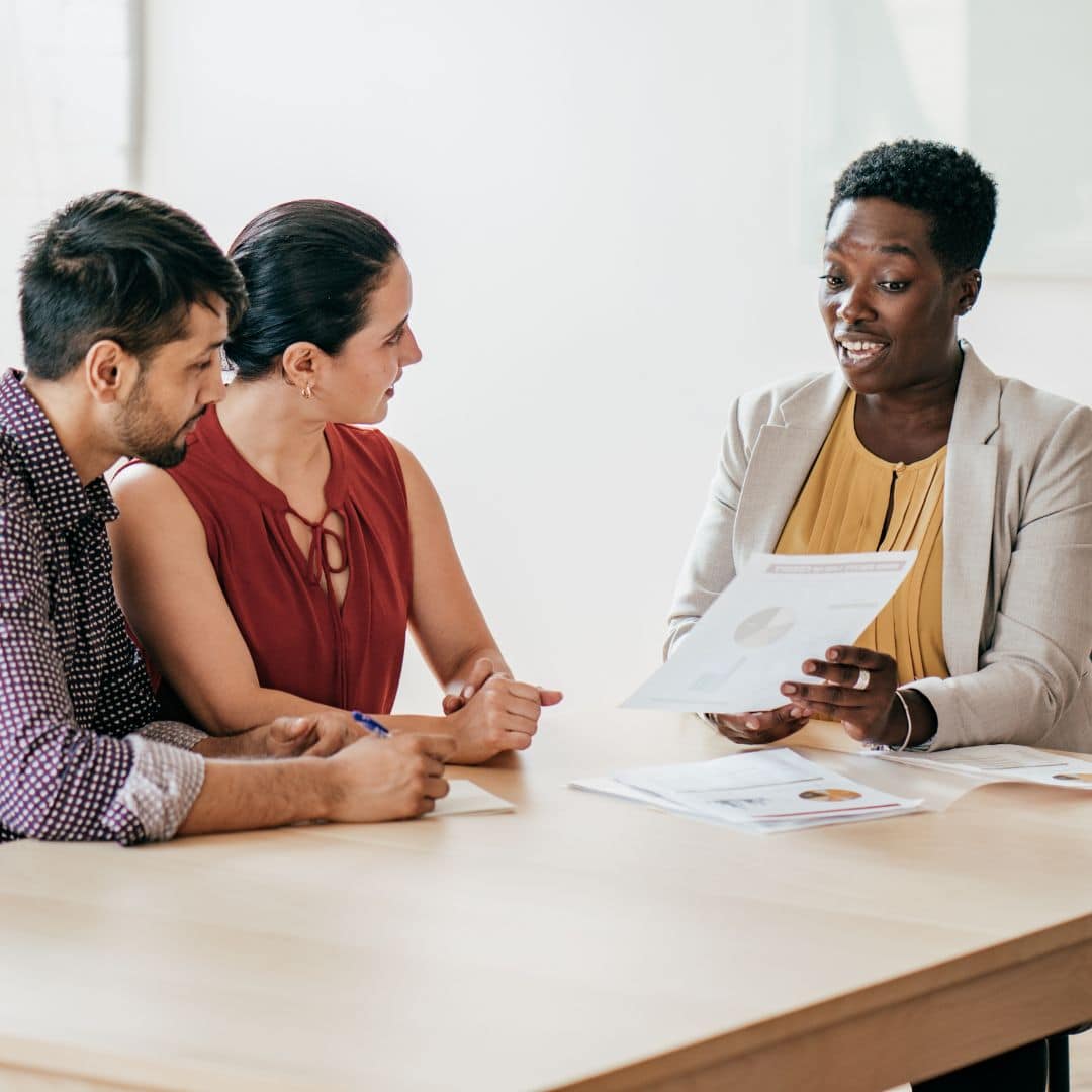 Business meeting with three professionals discussing documents at a table, emphasizing team collaboration and communication.