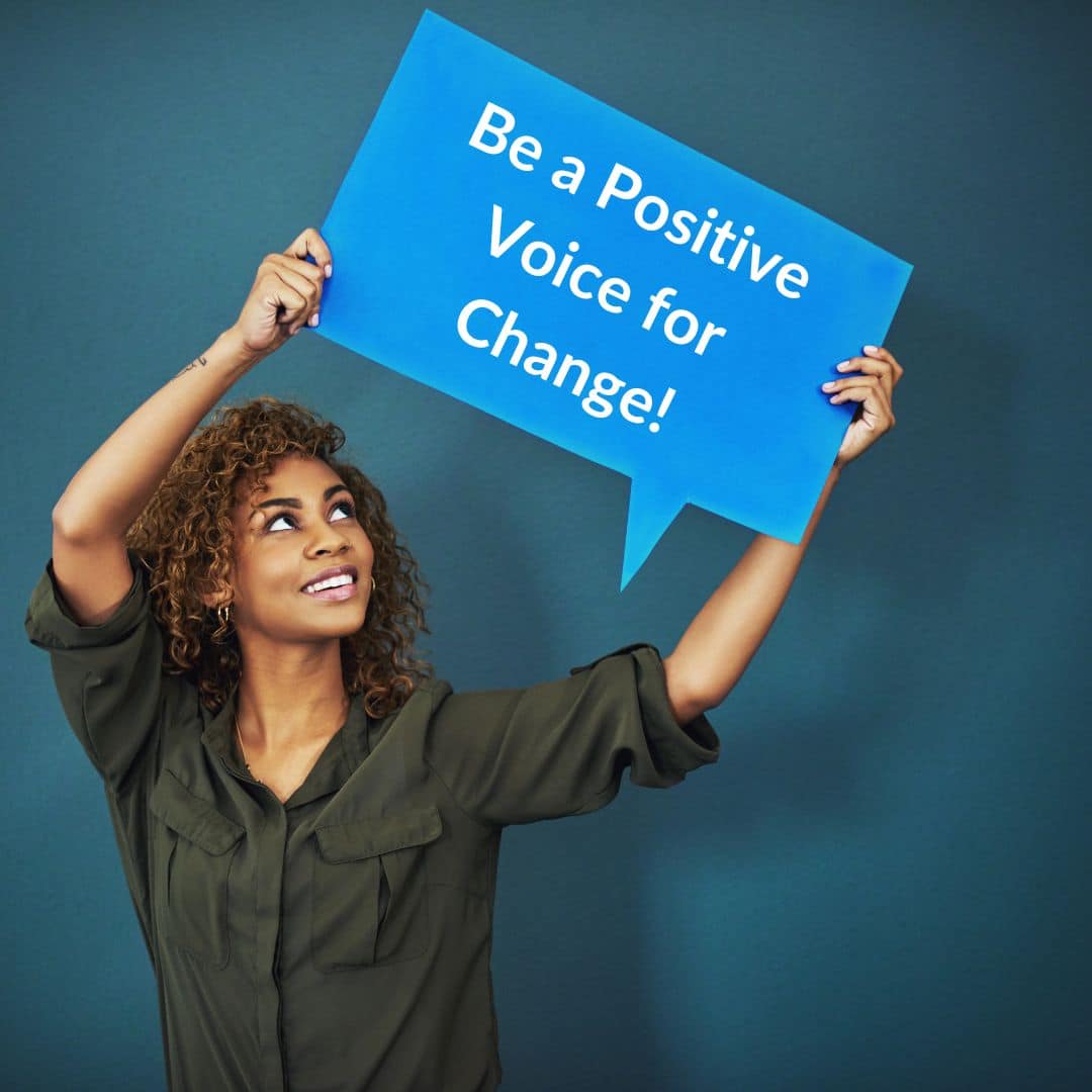 Smiling woman holding a blue "speech bubble" that says "be a positive voice for change"