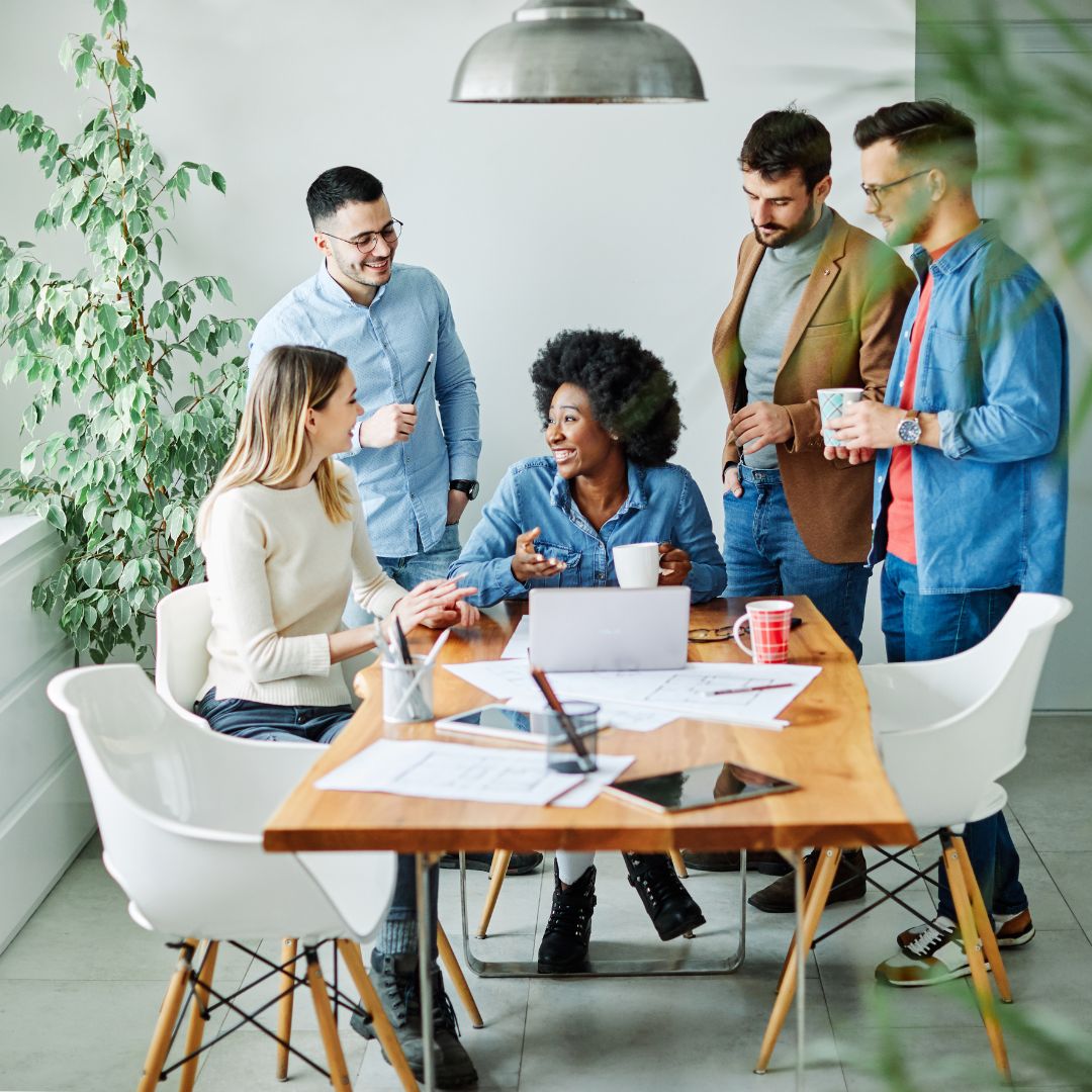 A diverse small business team collaborating on a project, sitting at a table with plants behind them