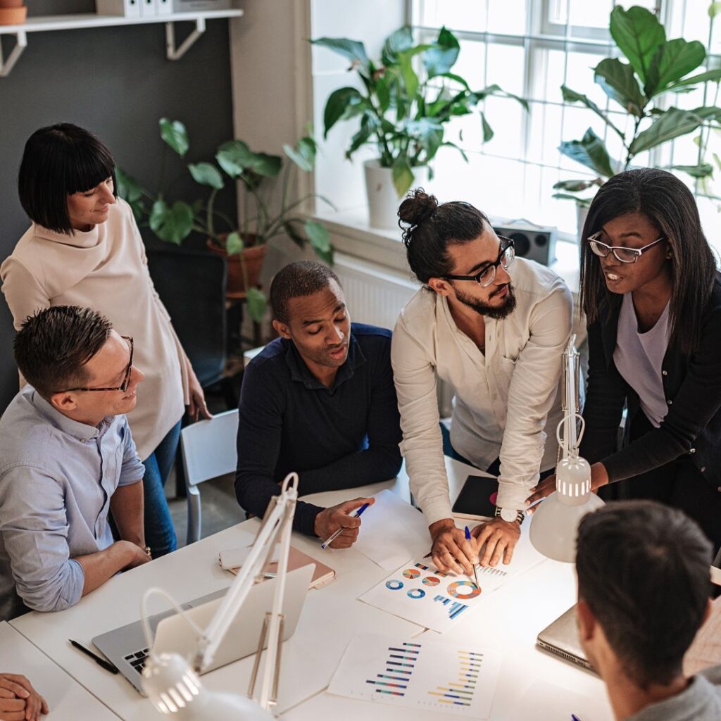 Group of diverse professionals collaborating on a DEI strategy plan, analyzing charts and graphs during a workshop setting.