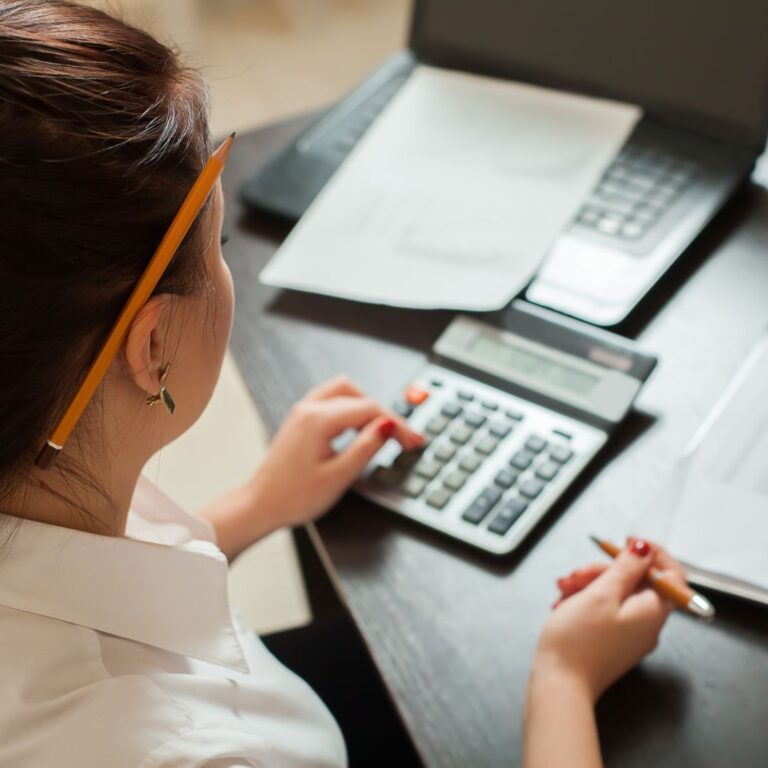 Woman using a calculator while reviewing billing documents, emphasizing streamlined billing processes for business efficiency.