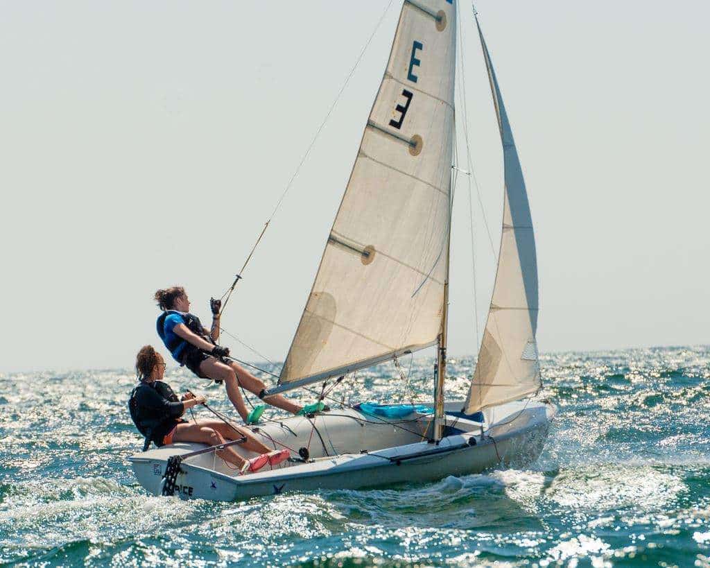 Sailboat with two young women navigating the ocean, showcasing teamwork and adventure in a vibrant coastal setting.