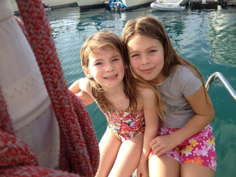 Two young girls smiling together on a boat, surrounded by water, reflecting a joyful family moment, connecting to Coach Pamela's personal life and family-oriented coaching approach.
