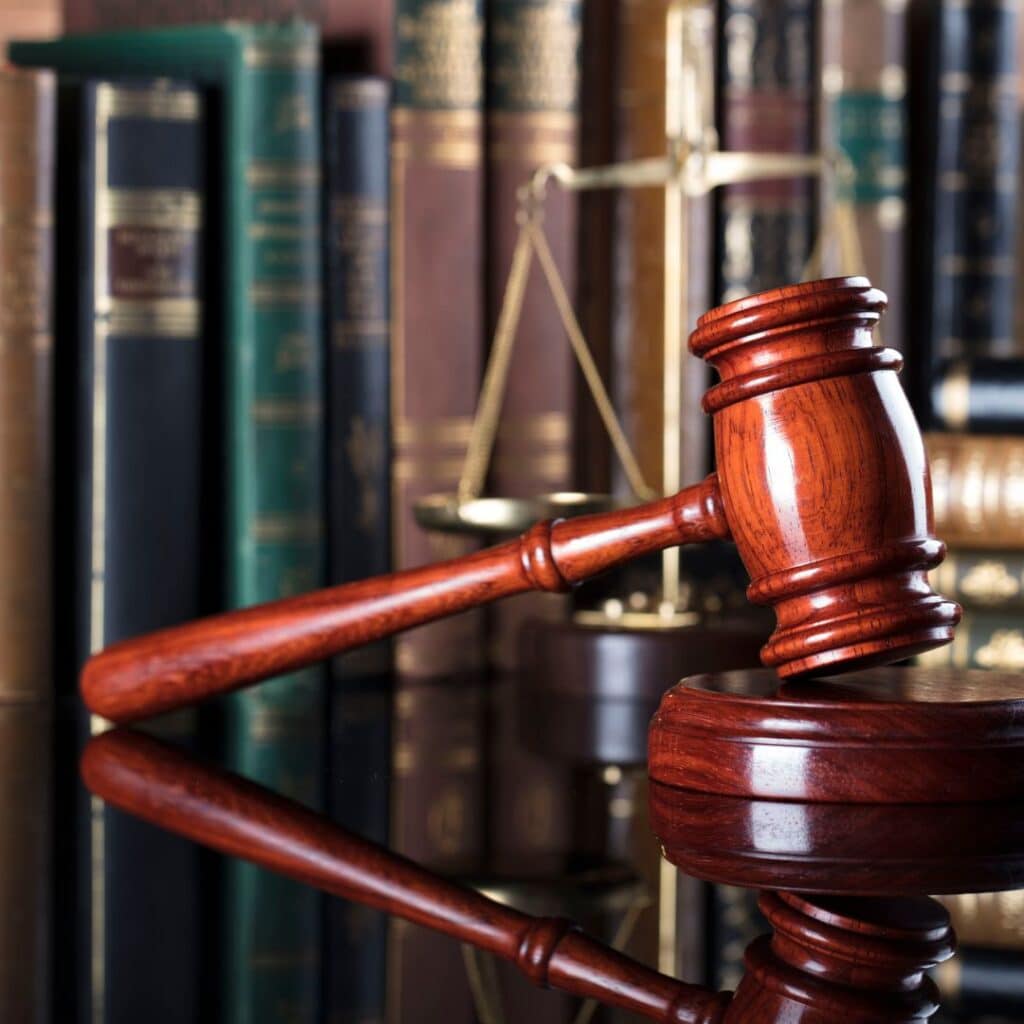 A gavel on a desk in front of a set of scales and law books.
