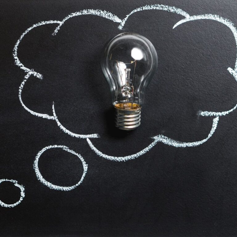 Light bulb surrounded by chalk-drawn thought bubbles on a dark background, symbolizing creativity and brainstorming in business growth and entrepreneurship.