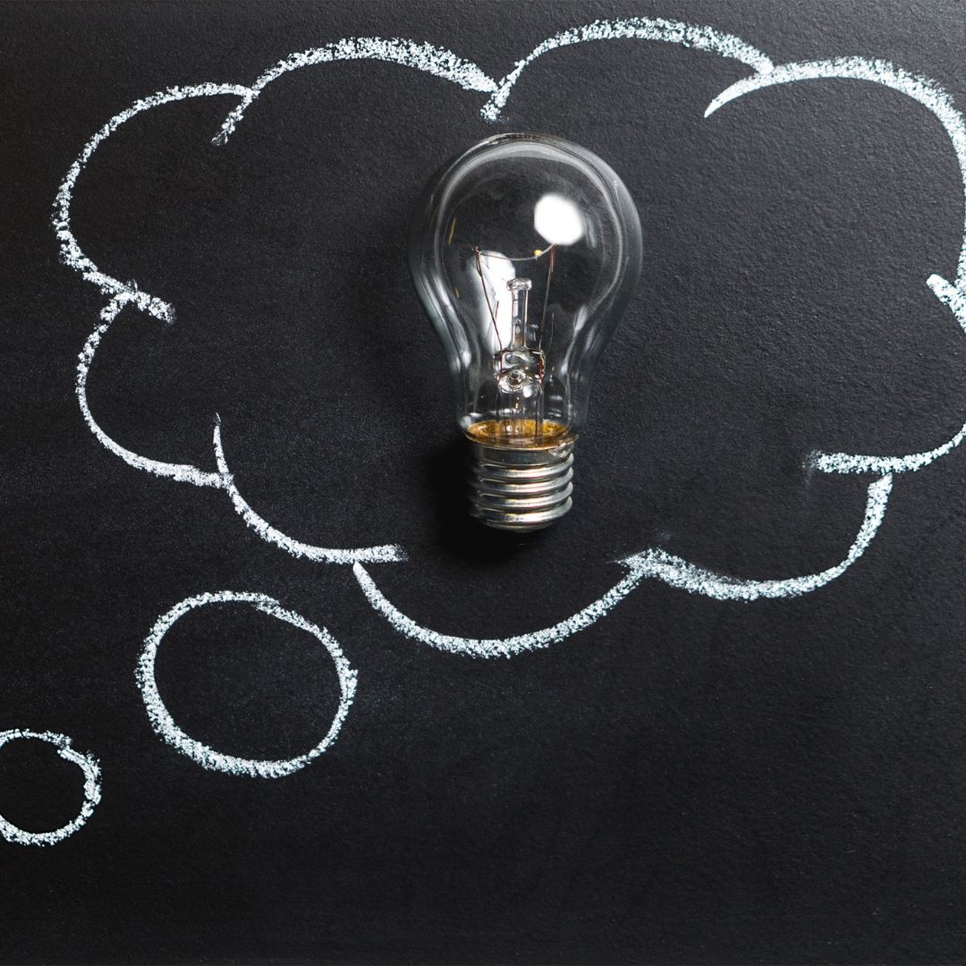 A flatlay of a light bulb on a chalkboard with a thought bubble drawn around it.