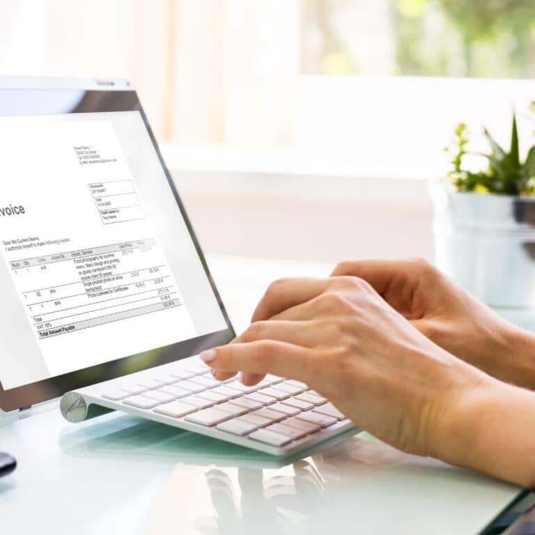 Person typing on a keyboard while reviewing an invoice on a tablet, emphasizing streamlined billing systems for small businesses.