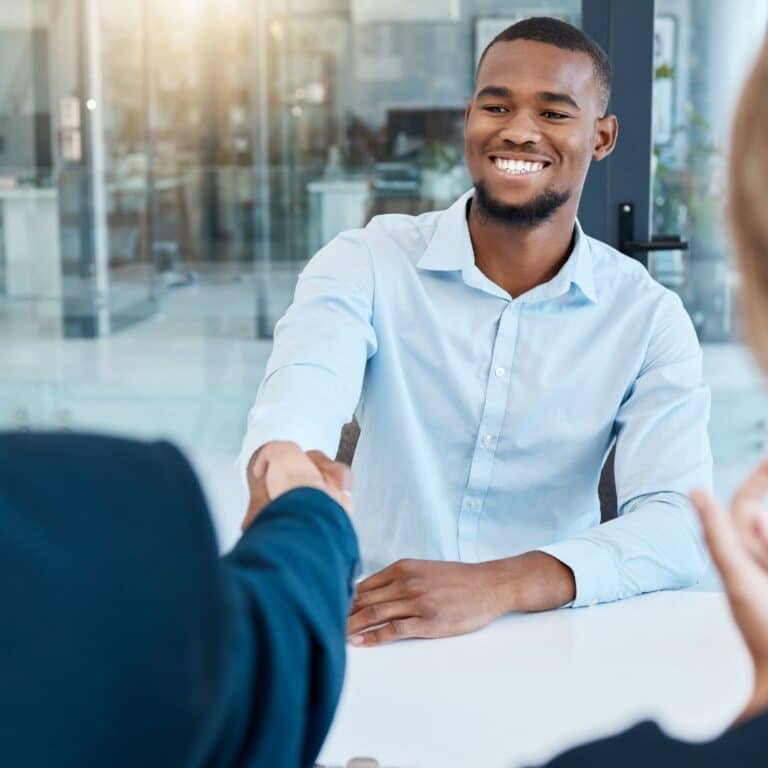A new hire shaking hands with his new manager across a desk.