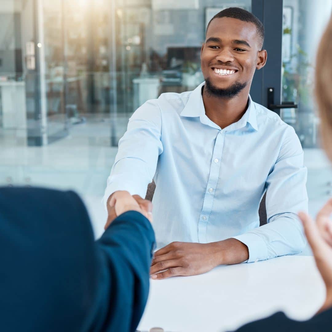 Smiling man in a light blue shirt shaking hands during a job interview, symbolizing hiring and onboarding processes for small businesses.