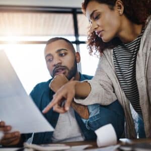 A man and a woman in an office discussing the details on a piece of paper.