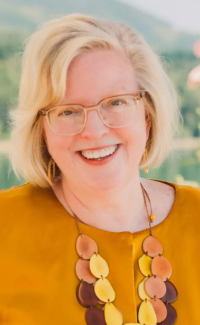 Smiling woman wearing glasses and a colorful necklace, representing empowerment and leadership in business coaching.