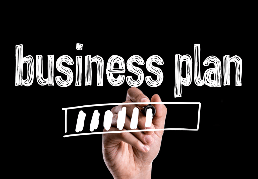 Hand writing "business plan" on a black background, emphasizing the importance of creating a business plan quickly.
