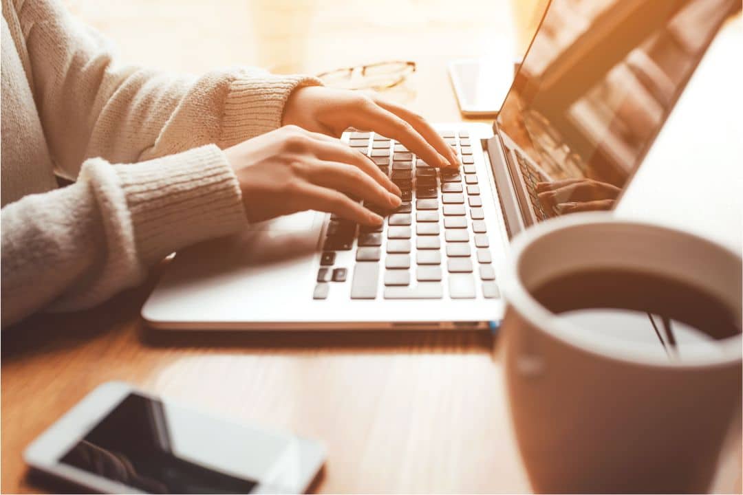Person typing on laptop with coffee cup and smartphone, illustrating operational efficiency and business systems improvement.