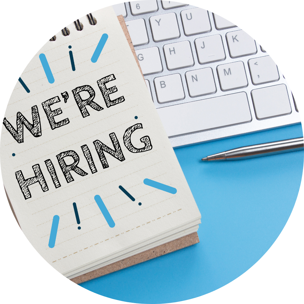 Notebook with "WE'RE HIRING" text and blue accents, next to a computer keyboard and pen, emphasizing recruitment for building a sales team.