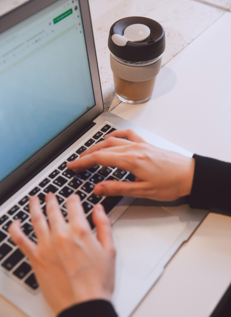 Person typing on a laptop while working on onboarding systems, with a coffee cup beside, illustrating productivity in a business training context.