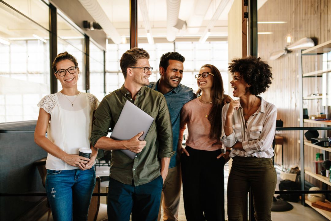 Group of diverse professionals smiling and engaging in conversation in a modern office setting, illustrating teamwork and effective communication in business.