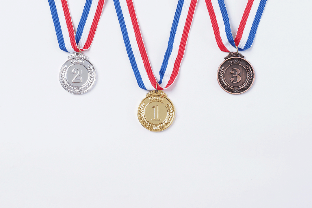 Gold, silver, and bronze medals hanging from red, white, and blue ribbons, symbolizing achievement and success in competitions, relevant to themes of celebration and business milestones.