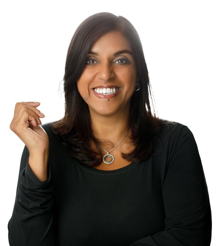 Melanie Seneviratne, Implementation and Systems Coach, smiling and gesturing, wearing a black top and necklace, representing her coaching services in business management and operations.