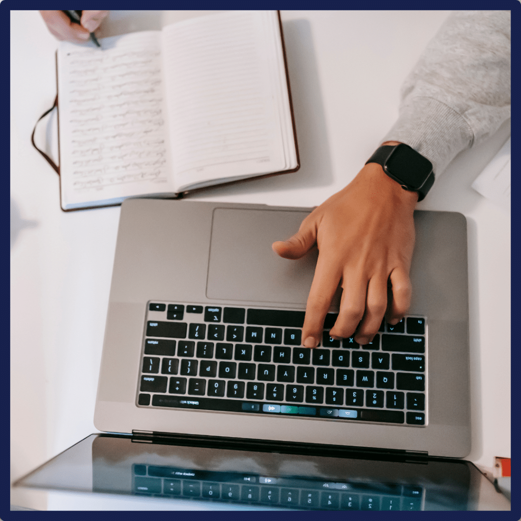 Person using a laptop with a notebook nearby, emphasizing financial management and productivity.